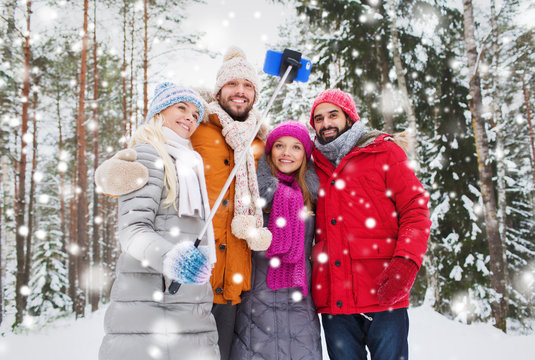 smiling friends with smartphone in winter forest