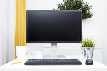 blank monitor and office accessories on table in bright interior