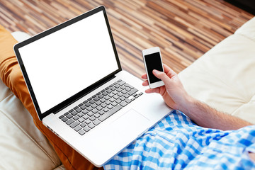 Laptop and smartphone mockup. Closeup of man holding laptop on his knees and smartphone in hand