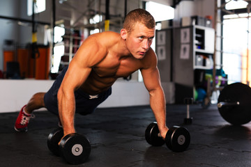 Fototapeta na wymiar Young man doing pushups on dumbbells at gym
