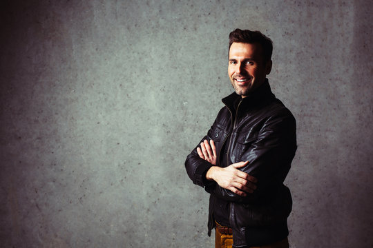 Happy man in leather jacket against concrete wall