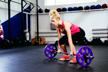 Fototapeta na wymiar Young woman training deadlift with barbells at gym