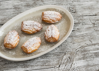 cookies madeleines with powdered sugar on oval plate on a light wooden surface
