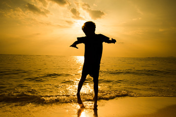 Silhouette of llittle boy jumping over the beach wave