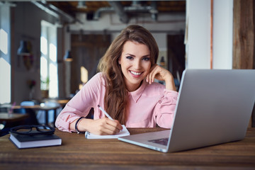 Happy female student at cafe with laptop and notepad