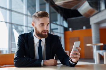 Stylish hipster with suit browsing his smartphone at modern offi