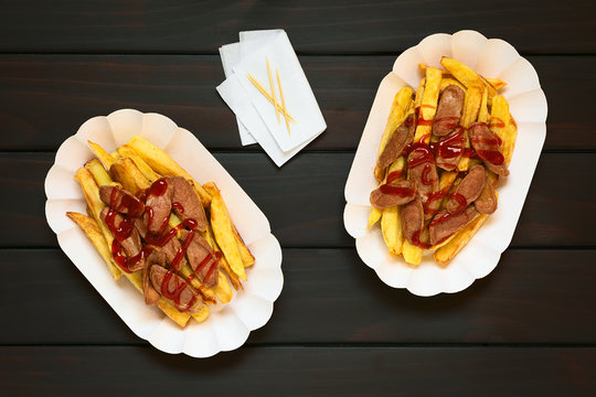 Salchipapas made of French fries and fried sausage, a traditional fast food in South America, photographed overhead on dark wood with natural light