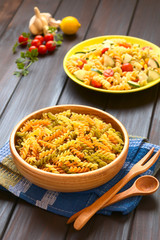 Raw tricolor fusilli or rotini pasta (traditional, tomato and spinach taste) with pasta salad in the back, photographed with natural light (Selective Focus, Focus one third into the pasta)
