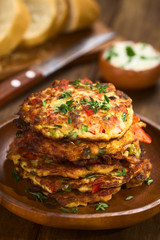 Vegetable and egg fritter made of zucchini, red bell pepper, eggs, green onions and thyme piled on a wooden plate (Selective Focus, Focus on the front of the thyme sprig on the top of the fritters)