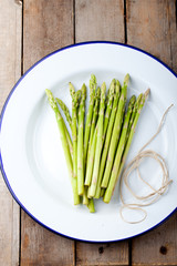 Asparagus sprouts on a white enamel plate.