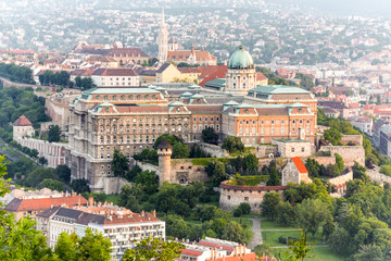 Fototapeta premium A panoramic aerial view of Buda Castle perched atop a hill overlooking Budapest with historic buildings and red rooftops under a soft hazy sky, the grand royal palace complex in central Europe.