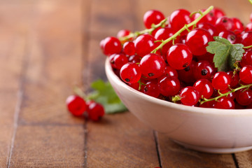 Fresh red currants in bowl on wooden table close up