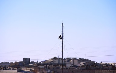 Technician service man Working On A Telecommunication Tower above the roofes of the city