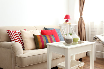 Beige sofa with beautiful pillows and decorative vases on the table in front of it in the room
