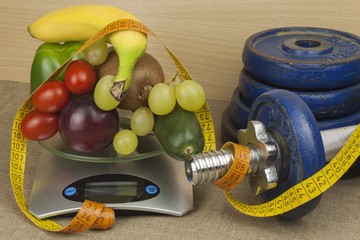 Chrome dumbbells surrounded with healthy fruits and vegetables on a table. Concept of healthy eating and weight loss. Diet for athletes.
