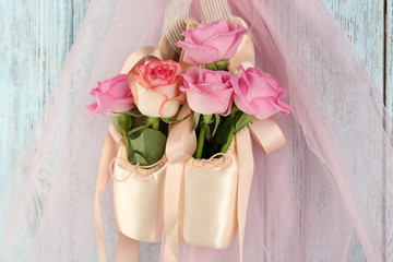 Decorated ballet shoes with roses in it hanging on blue wooden background