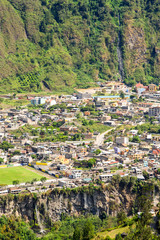 Obraz premium An aerial view of the town of Banos de Agua Santa perched on a steep mountain slope with colorful roofs surrounded by dense green vegetation and rugged cliffs in Tungurahua Province, Ecuador.