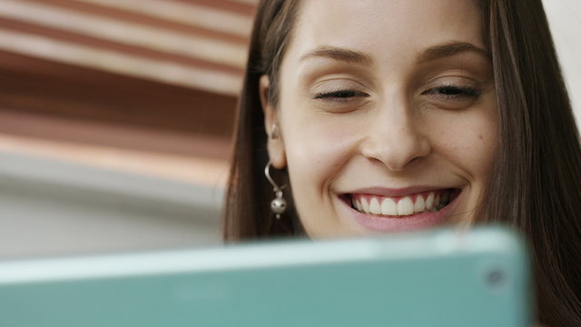 4K Close shot of young woman smiling as she reads her digital tablet, in slow motion