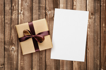 Gift box and blank greeting card on wooden background