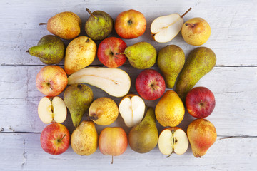 apples and pears whole and halved shot from above on white wooden boards
