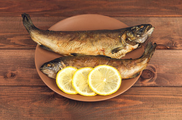 On the wooden table is a plate with two baked fish trout