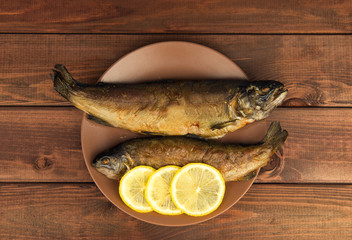 On the wooden table is a plate with two baked fish