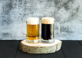 Light and dark beer in mugs on wooden board, grunge backdrop.