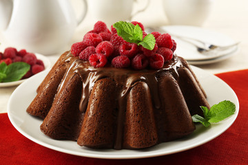 Tasty chocolate muffin with glaze and raspberries on table close up