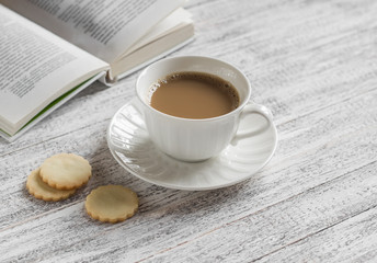 Cup of coffee, biscuits and a book on a white wooden surface