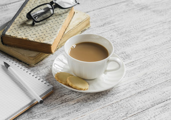 A stack of books, open  clean notepad, glasses and a cup of cocoa on a white wooden table. The concept of education and training