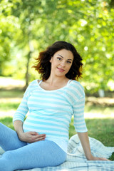 Fototapeta premium Cute happy pregnant woman on white blanket in the park