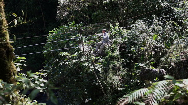 Wide and long shot of a man in an old cable car crossing a deep ravine in a very green rain-forest type environment in Ecuador coming towards the viewer.