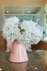 white plastic flowers in pink flower vase on the rattan weave