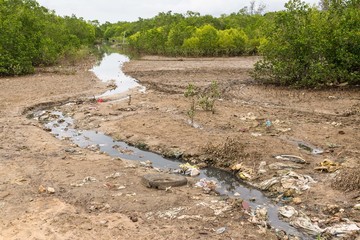 Heavily polluted water stream filled with rubbish running throug - 94470150