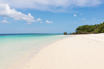 Pristine white tropical beach with blue sea and lush vegetation