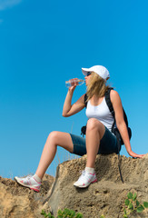 Fototapeta na wymiar Female hiker rests on the rock and drinks water.