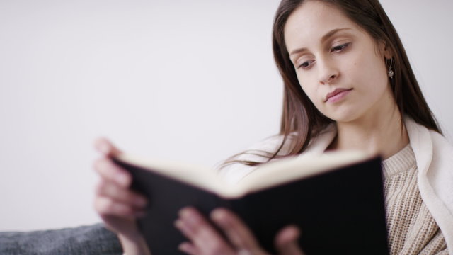 4K Young woman at home in a blanket reading a book on the couch