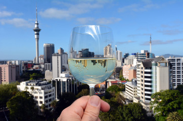 Mans hand holds a white wine glass against Auckland skyline
