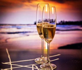 Champagne glasses on tropical beach at sunset - exotic New Year