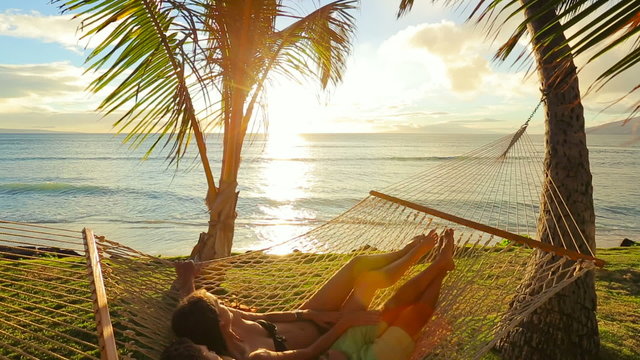 Romantic couple relaxing in tropical hammock at sunset