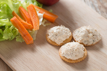 Cracker with tuna spread topping on wood cutting board.