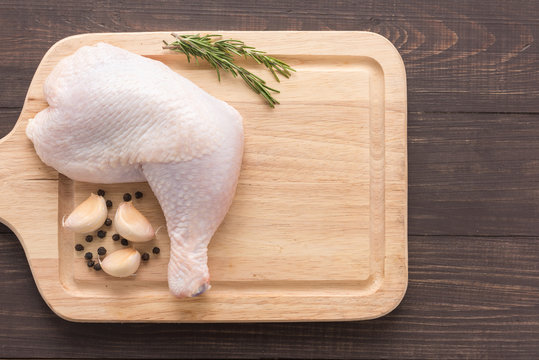 Raw chicken leg on cutting board on wooden background