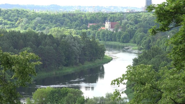 Monastery buildings between forest and Neris river flowing. Vilnius city in distance. Zoom in shot. 4K
