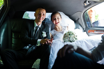 happy wedding couple sitting in limo - obrazy, fototapety, plakaty