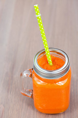 Healthy carrot smoothie in a jar with tube wooden background