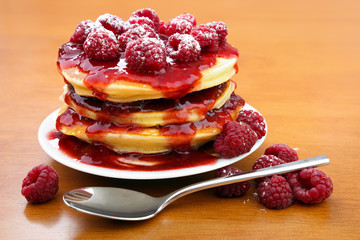 Stack of american pancakes with strawberry jam and fresh raspberry fruits on white plate with spoon