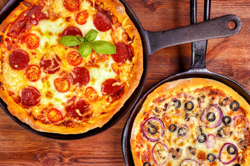 Two fresh pan pizzas on iron skillets , wooden background , top view - 94498398
