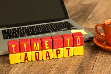 Time To Adapt written on a wooden cube in front of a laptop