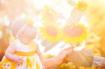 beautiful baby girl near yellow sunflowers on field