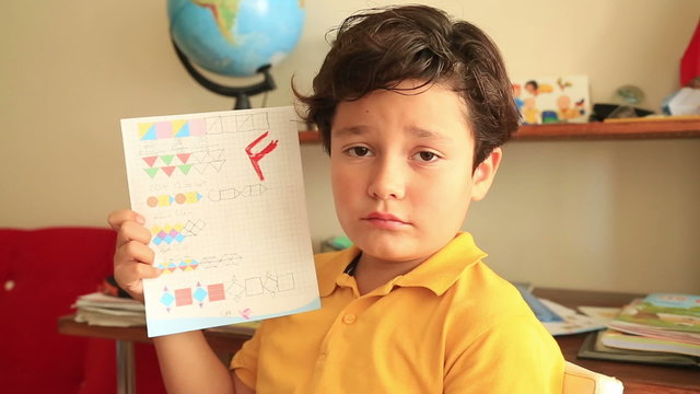 Unhappy little student  holding school paper with F grade